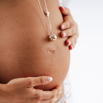 Chiama Angeli in oro giallo adagiato sul pancione di una futura mamma in dolce attesa
